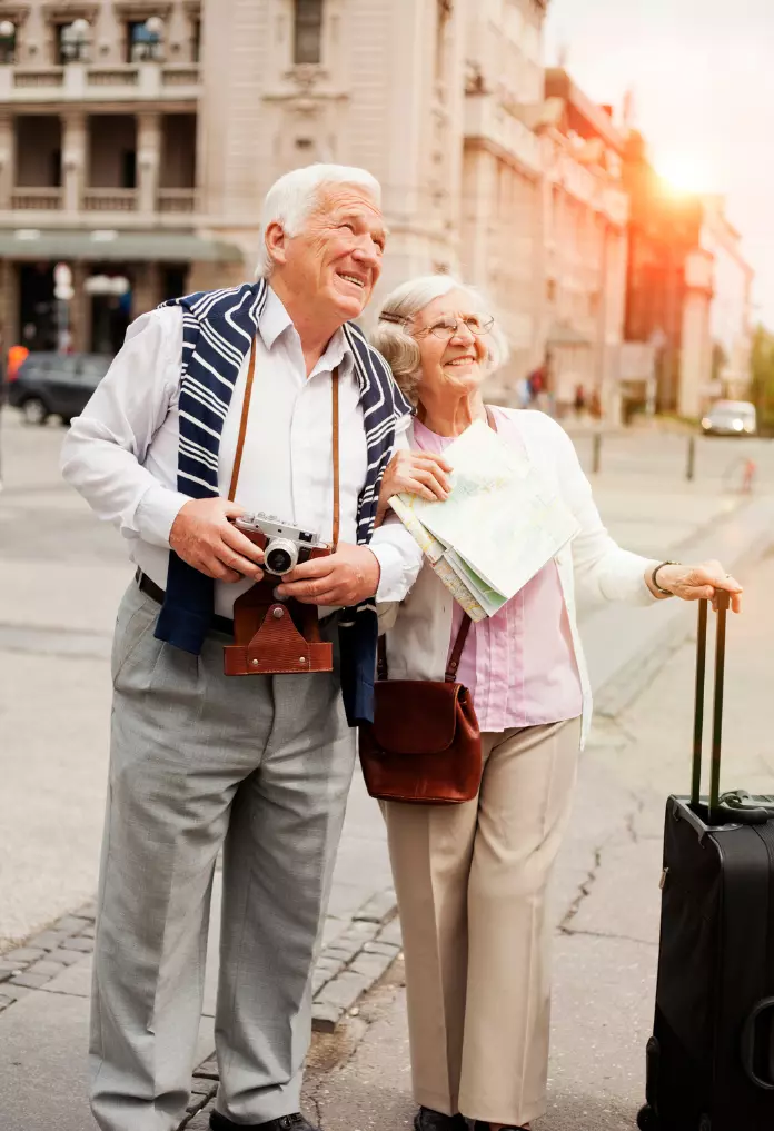Senior couple standing with suitcase on the street and looking around