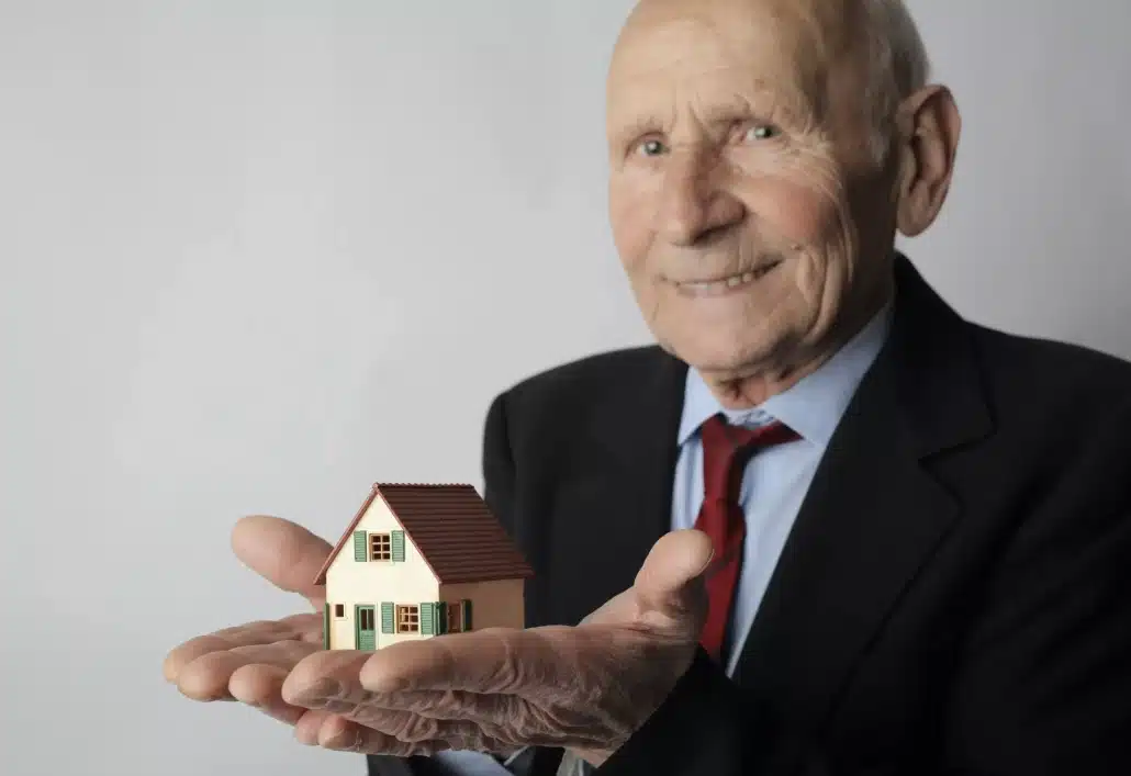 Old man in black suit holding a miniature wooden house