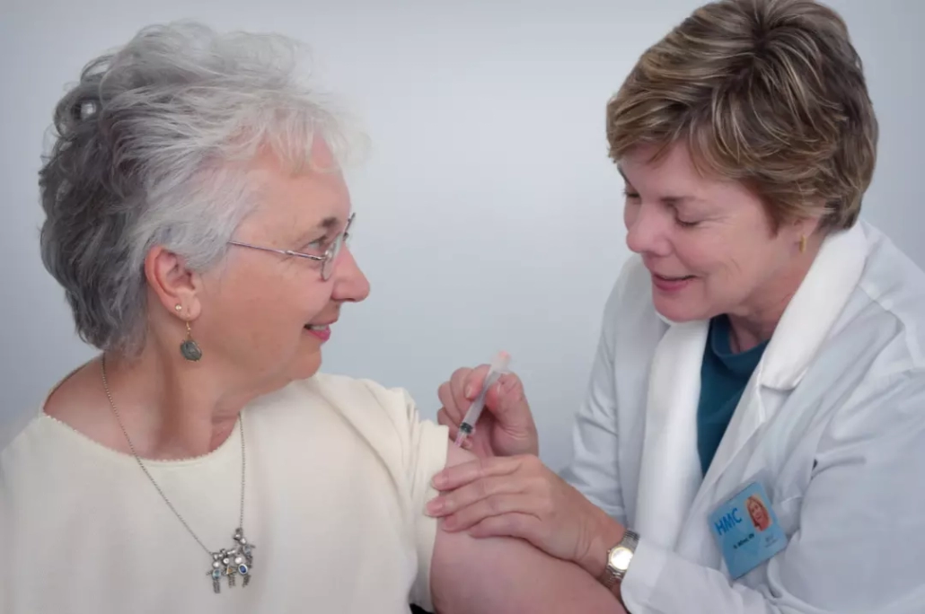 Doctor injecting an old woman in her shoulder.