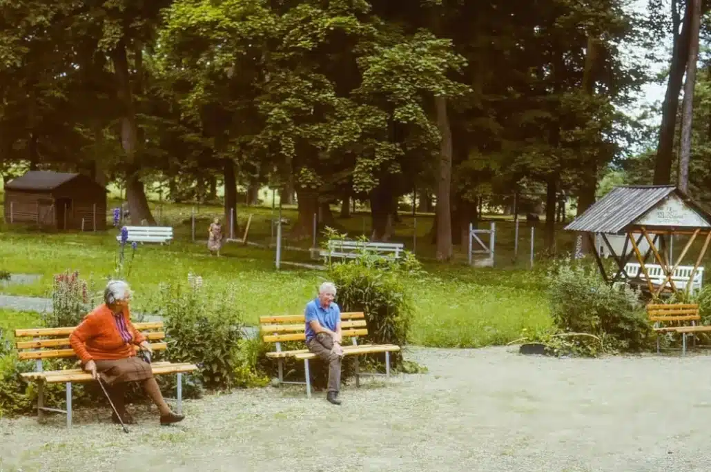 Senior man and woman sitting on a wooden bench in a retirement facility.