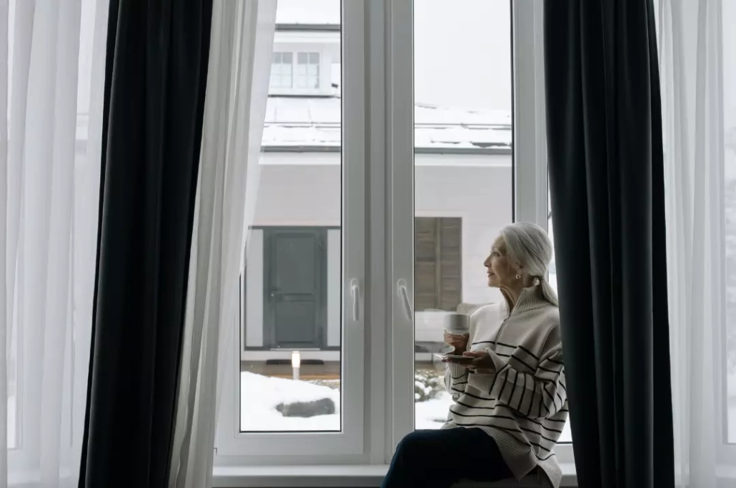An elderly woman sitting beside the glass window.
