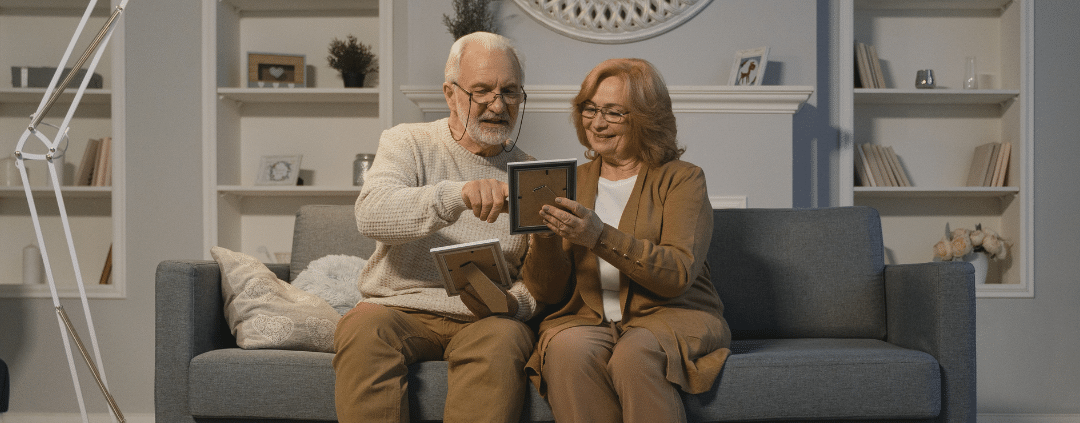 Elderly couple sitting on a couch while looking at the framed pictures.