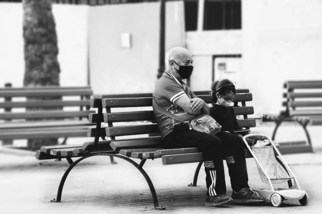 Elderly man sitting on a wooden bench with his granddaughter.