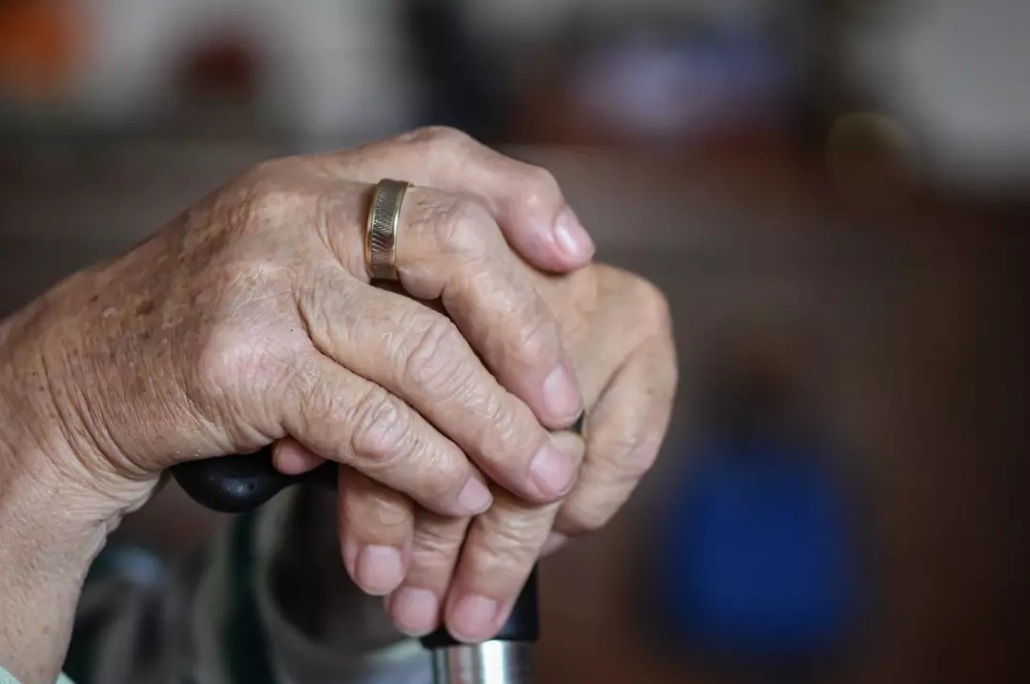Hands of an old person wearing a ring and holding a cane.