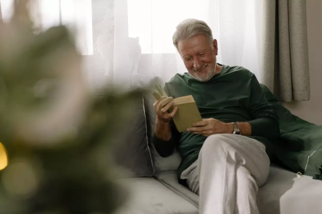 Happy old man reading a book while sitting on a sofa.