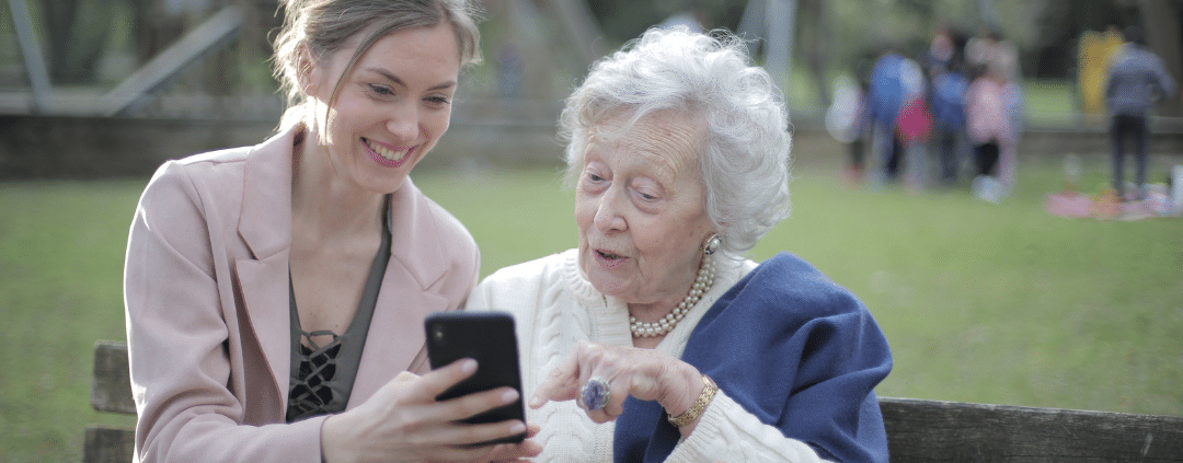 Mother and daughter sitting on a wooden bench in the park while using a phone.