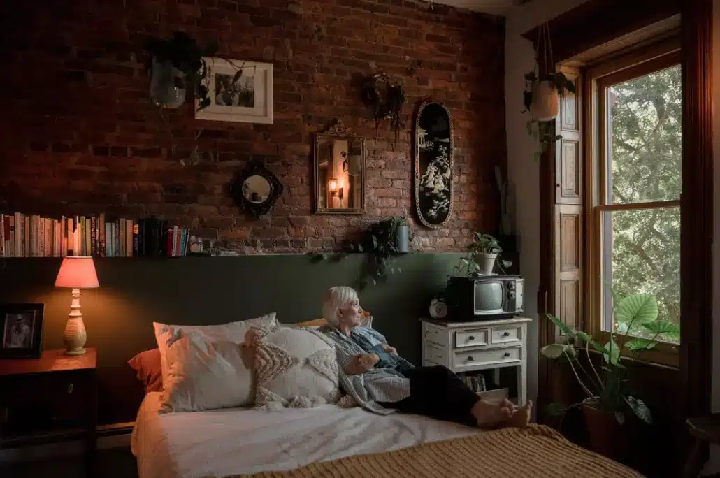 Old woman sitting on the bed looking at the window.