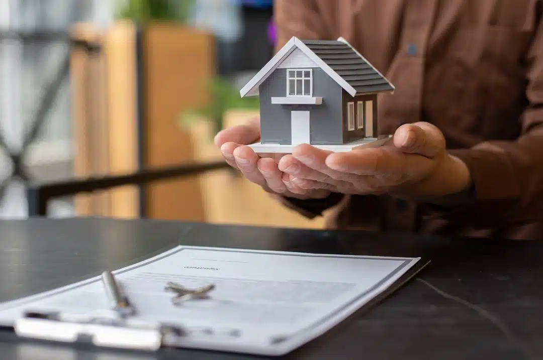 How to Reduce Assets for Aged Care: 7 Legit Strategies (2026 Guide) Person carrying a wooden miniature house after signing a contract.