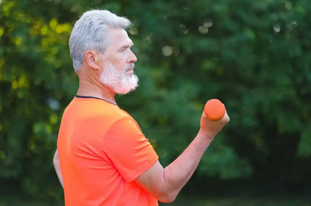 Old man in orange shirt exercising with dumbbells.