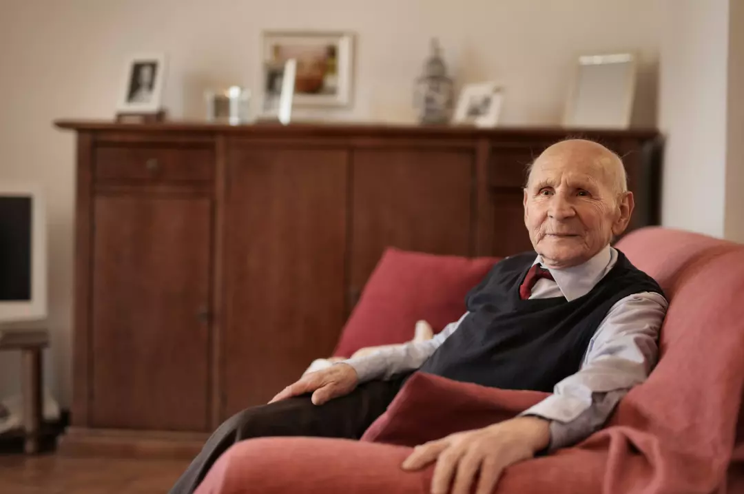 Old man sitting on a red sofa.