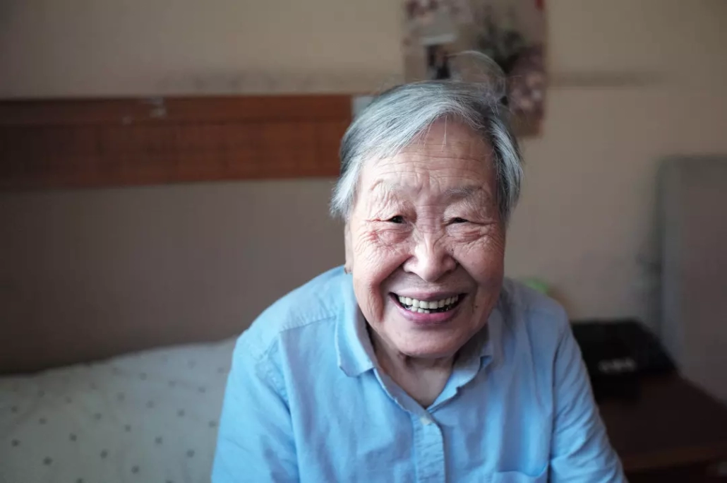 Old woman smiling while sitting on bed.
