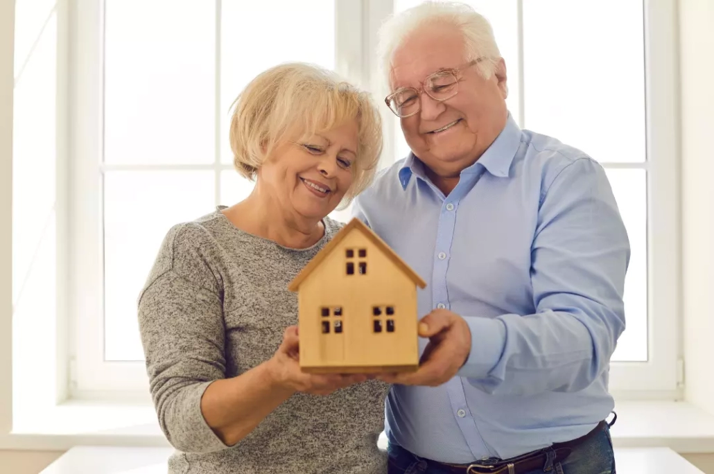 Senior couple standing by the window carrying a small wooden house.