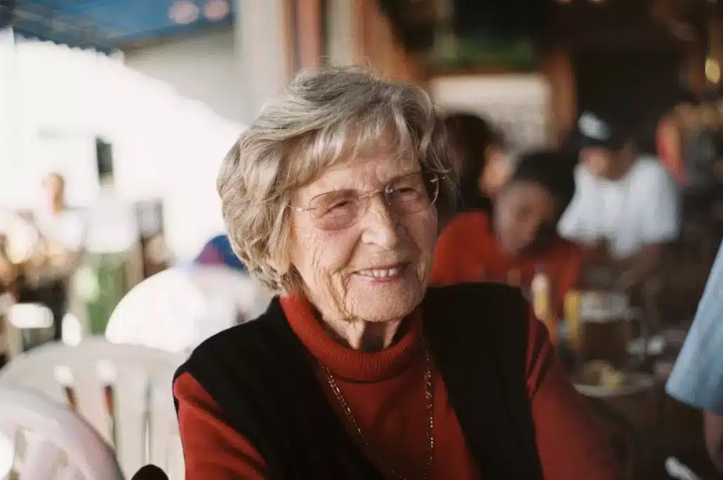 Smiling old woman in red sweater and black vest.