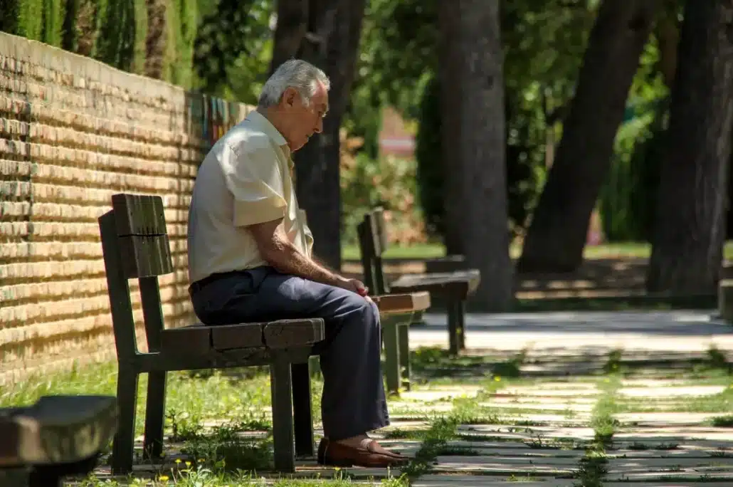 Senior man sitting on a concrete bench in the sidewalk.