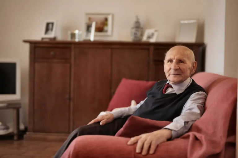 Old man in formal suite sitting on a red sofa.