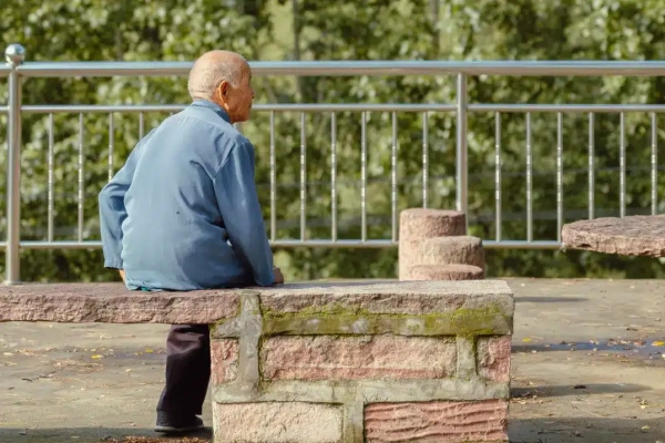 Old man in blue sleeve sitting on a concrete bench.